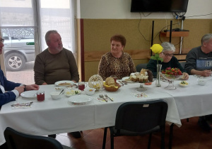 Seniorzy z Klubu Senior+ wraz z Panem Wójtem Gminy Lubochnia siedzą przy wielkanocnym stole.