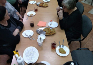 Seniorzy będący uczestnikami Klubu "Senior+" w Brenicy siedzą przy stole podczas poczęstunku w ramach zajęć kulinarnych.