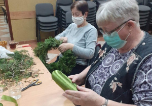 Seniorki będące uczestnikami Klubu "Senior+" siedzą przy stole podczas wykonywania ozdoby świątecznej.