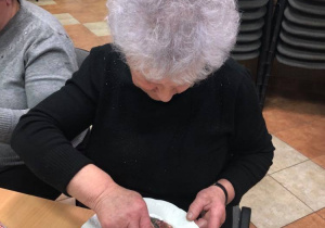 Seniorka będąca uczestnikiem Klubu "Senior+" siedzi przy stole podczas wykonywania talerza techniką decoupage.