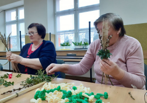 Seniorki przy stole podczas wykonywania palm wielkanocnych.
