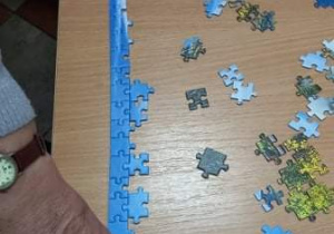 Seniorzy z Klubu "Senior+" układają puzzle.