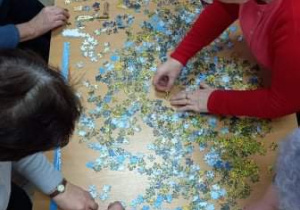 Seniorzy z Klubu "Senior+" układają puzzle.